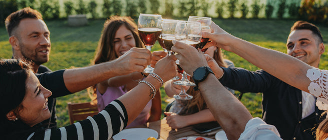 Welkom bij Wijnjuweel. Mensen zitten samen buiten en proosten met een glas wijn.